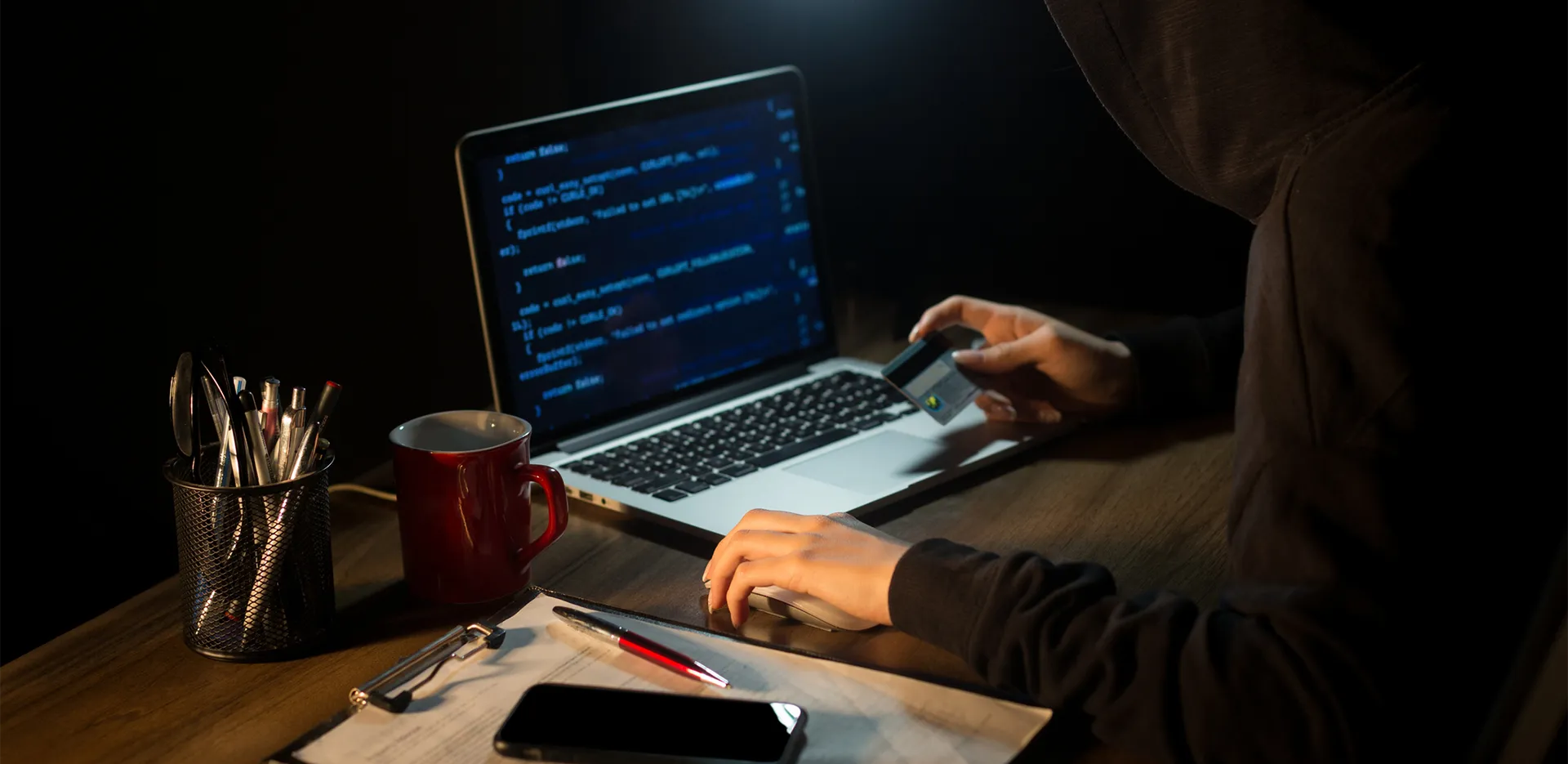 A person sitting in shadow looking at code on a laptop computer.