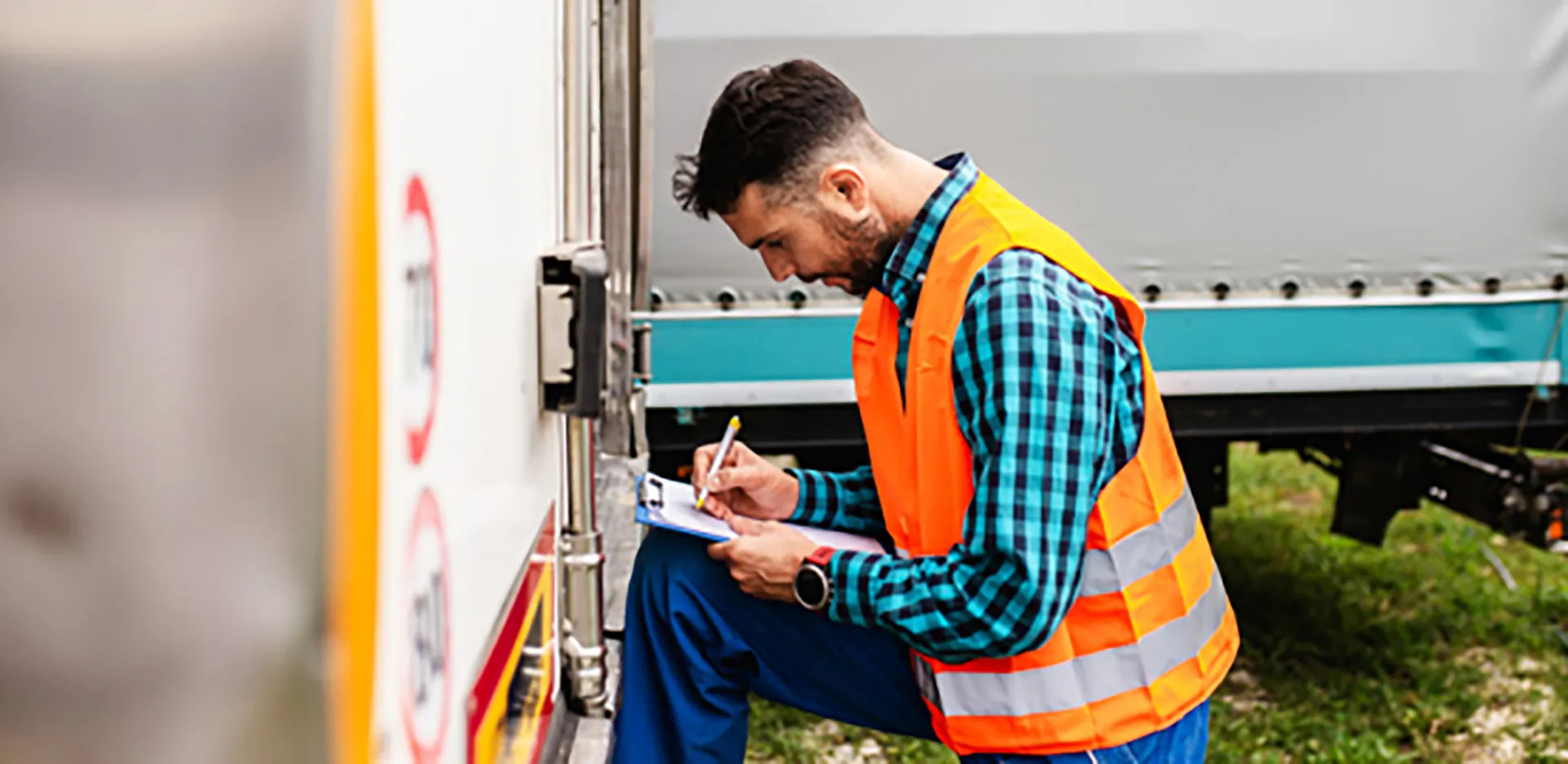 A contractor kneeling and taking notes on a clipboard.