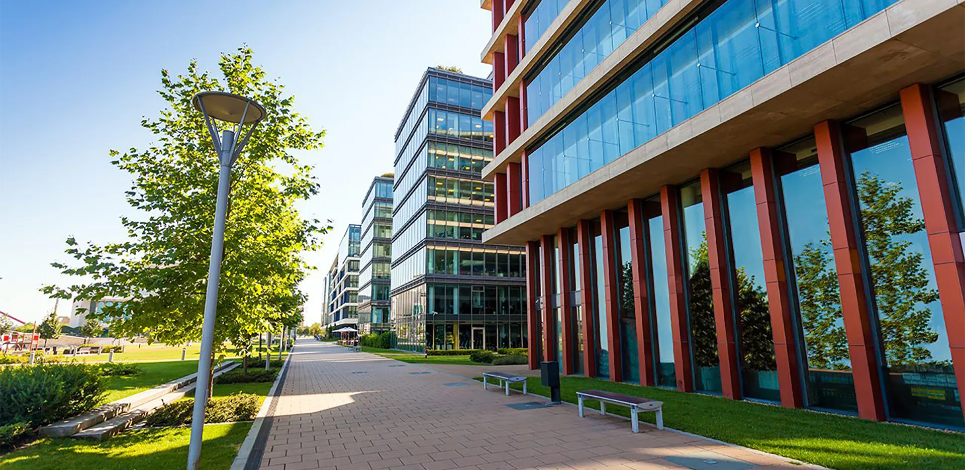 A series of office buildings next to a green lawn and brick sidewalk.