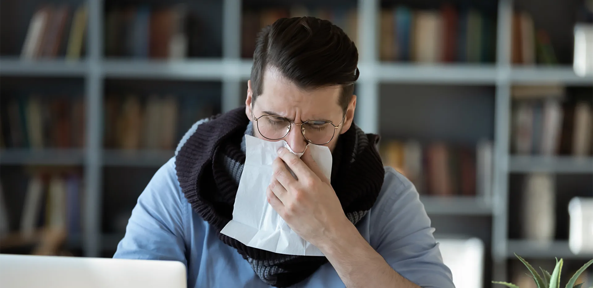 A professionally-dressed person wearing a cowl scarf and blowing their nose.