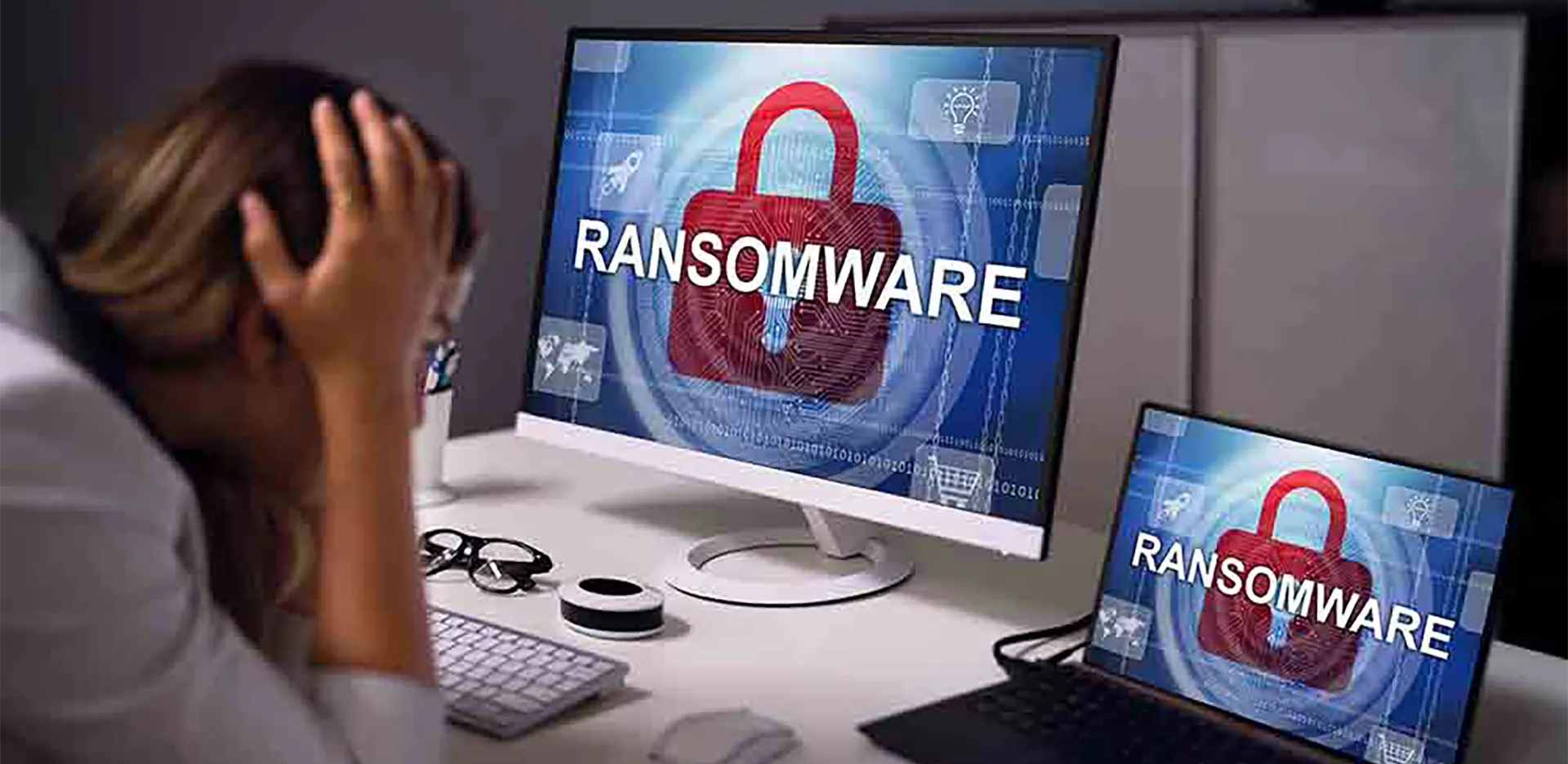 A person holding their head in their hands, staring at a computer screen that reads 'ransomware.'