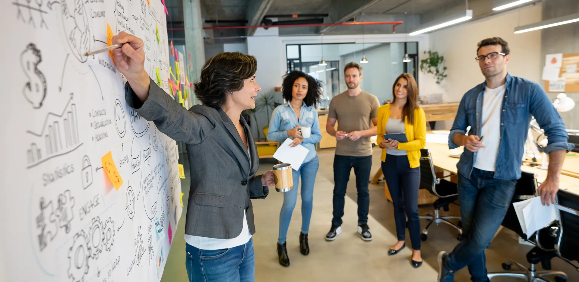 A group of professionals watching their colleague give a presentation in front of a whiteboard.