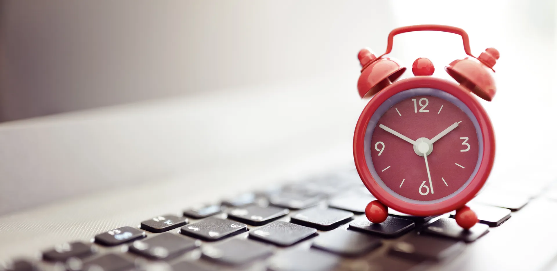 A red alarm clock rests on top of a computer keyboard.