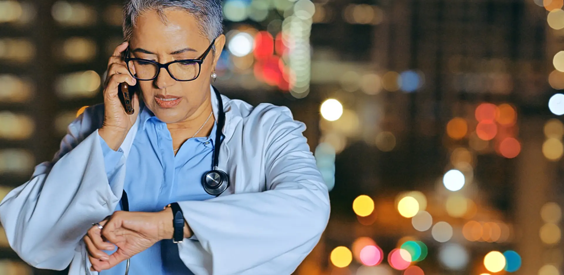 A doctor talking on a mobile phone and looking at her watch.