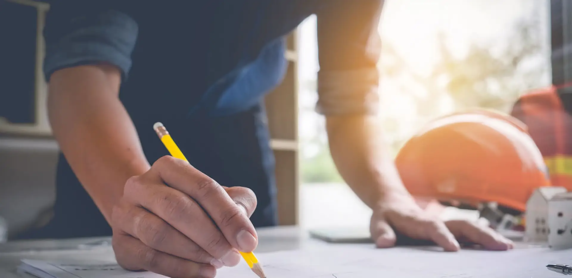 A contractor making notes with a pencil. There are tools and a hard hat in the background.
