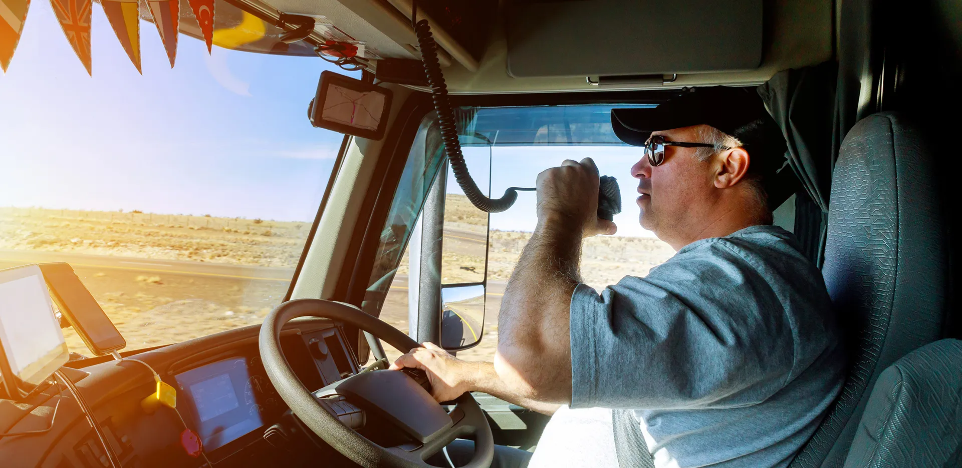A truck driver in a truck cab, driving and talking on a CB radio.