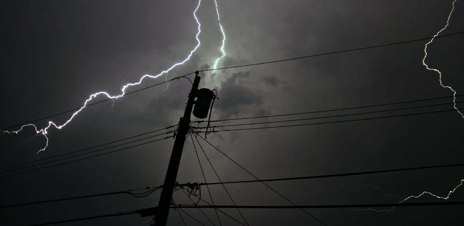 Powerlines backlit by lightning against a stormy sky.