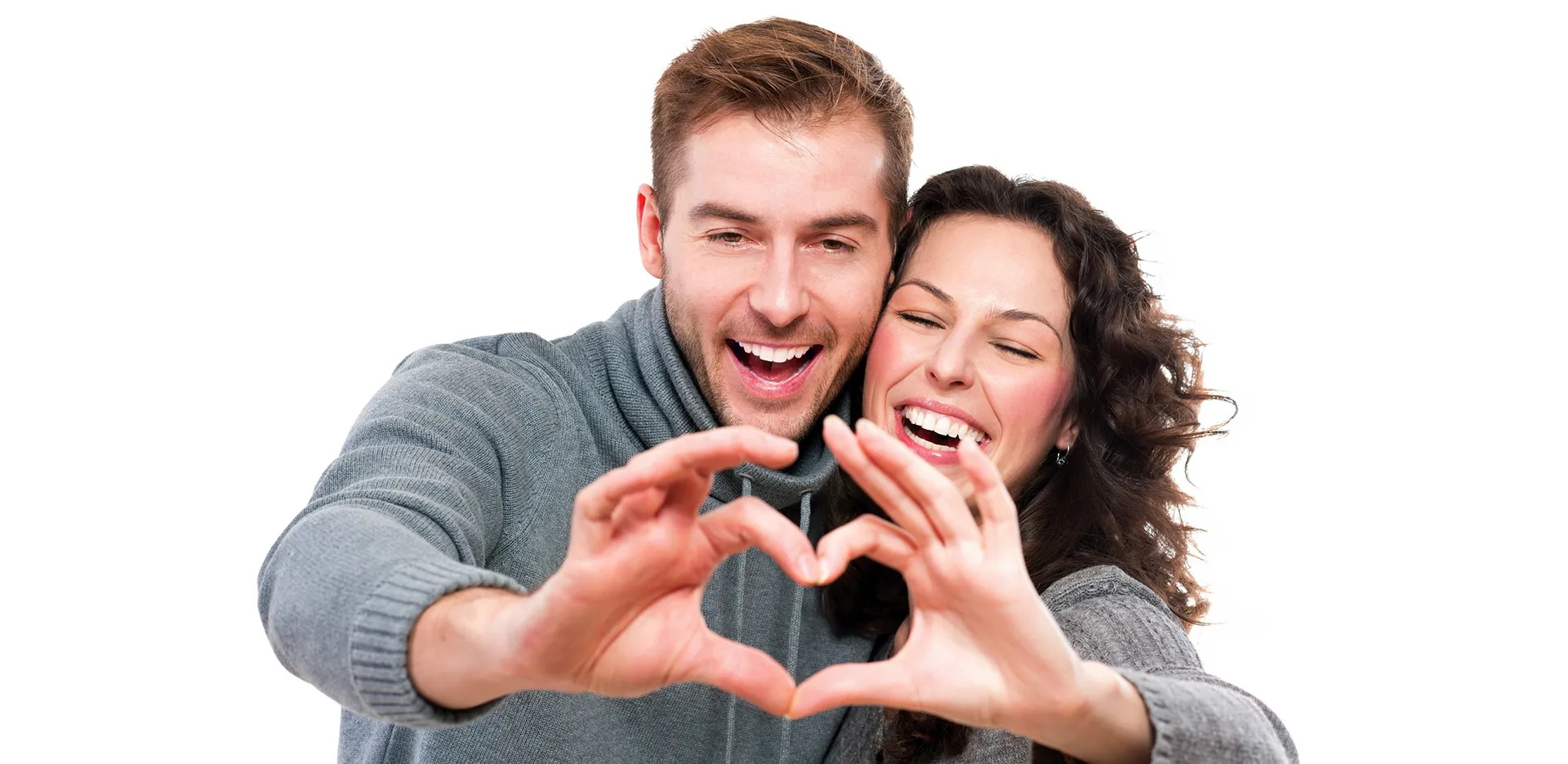 A couple smiling and making a heart with their fingers.