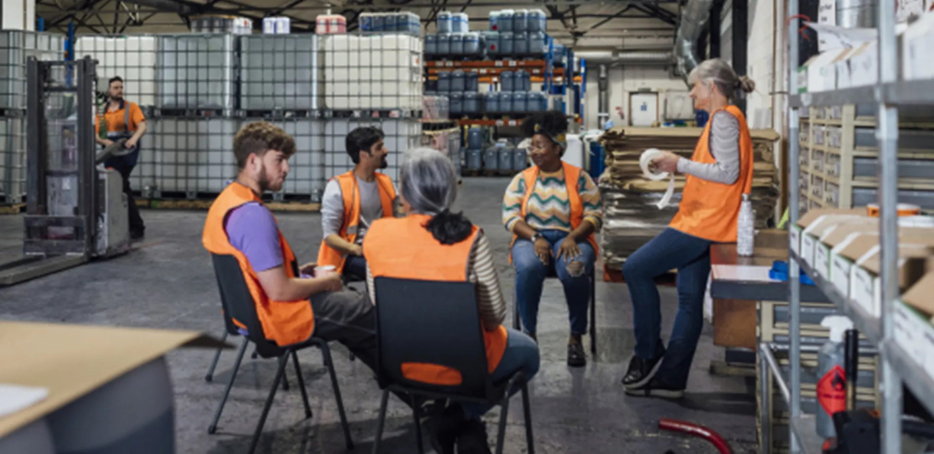A group of workers in safety vests sitting in a circle of chairs and talking to each other.