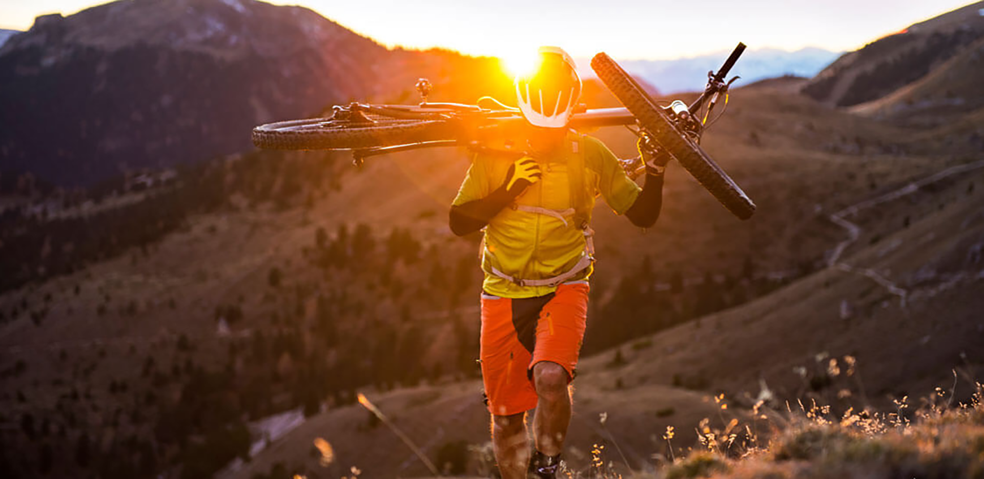 A cyclist walking up a mountain carrying their bike over their shoulder.