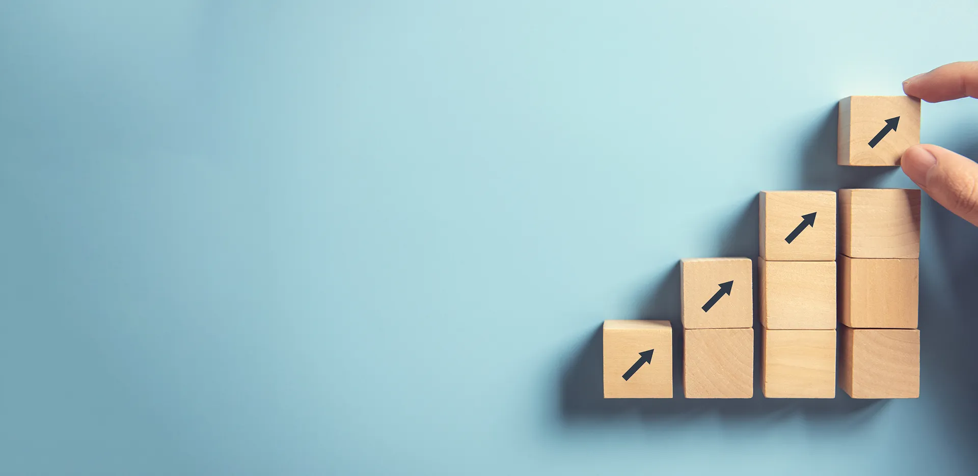A hand stacking wooden blocks to mimic a bar graph.