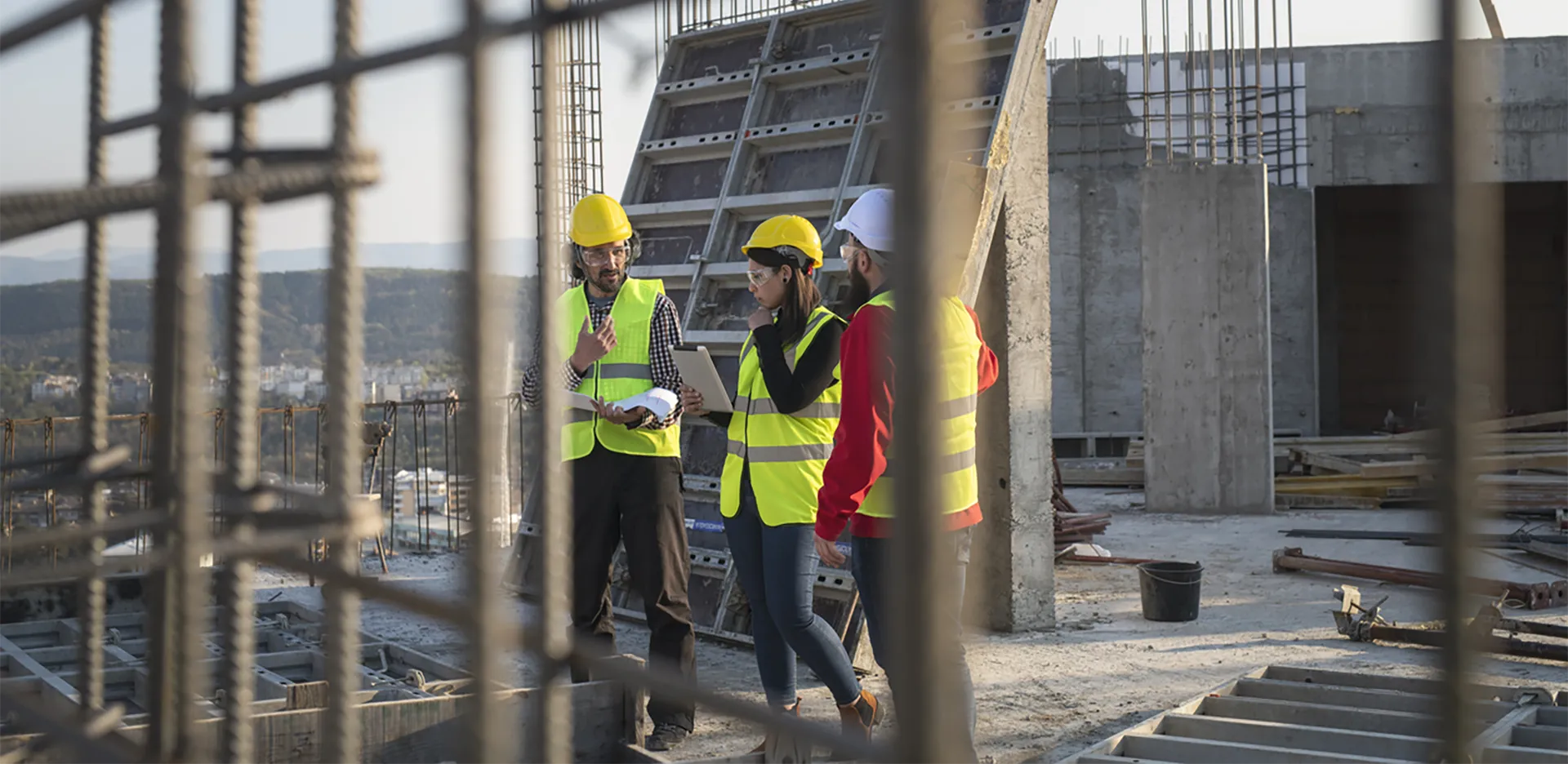 Three contractors standing on a roof surrounded by concrete and scaffolding.