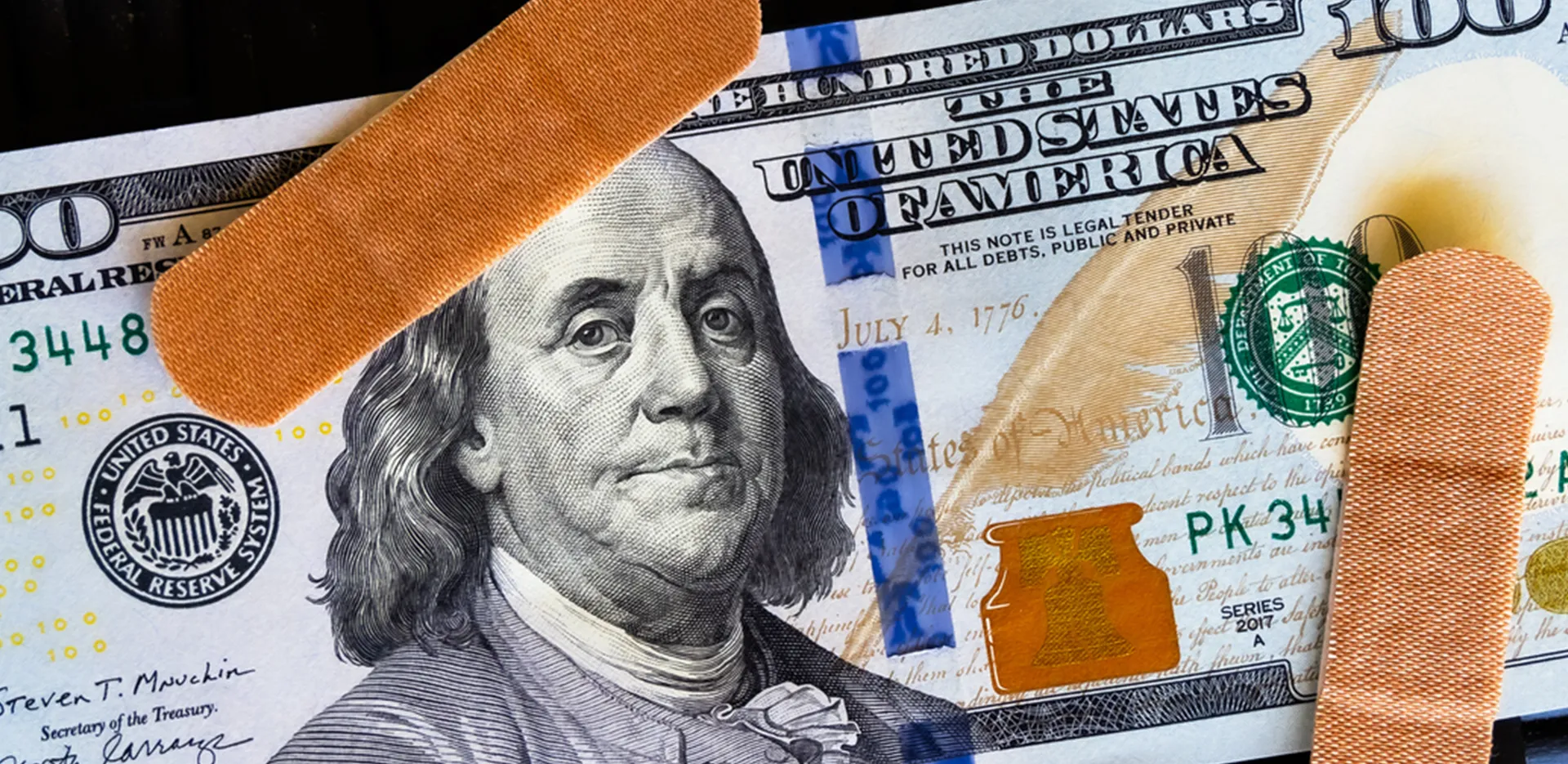 A 100 dollar bill with a couple band-aids on top of it.