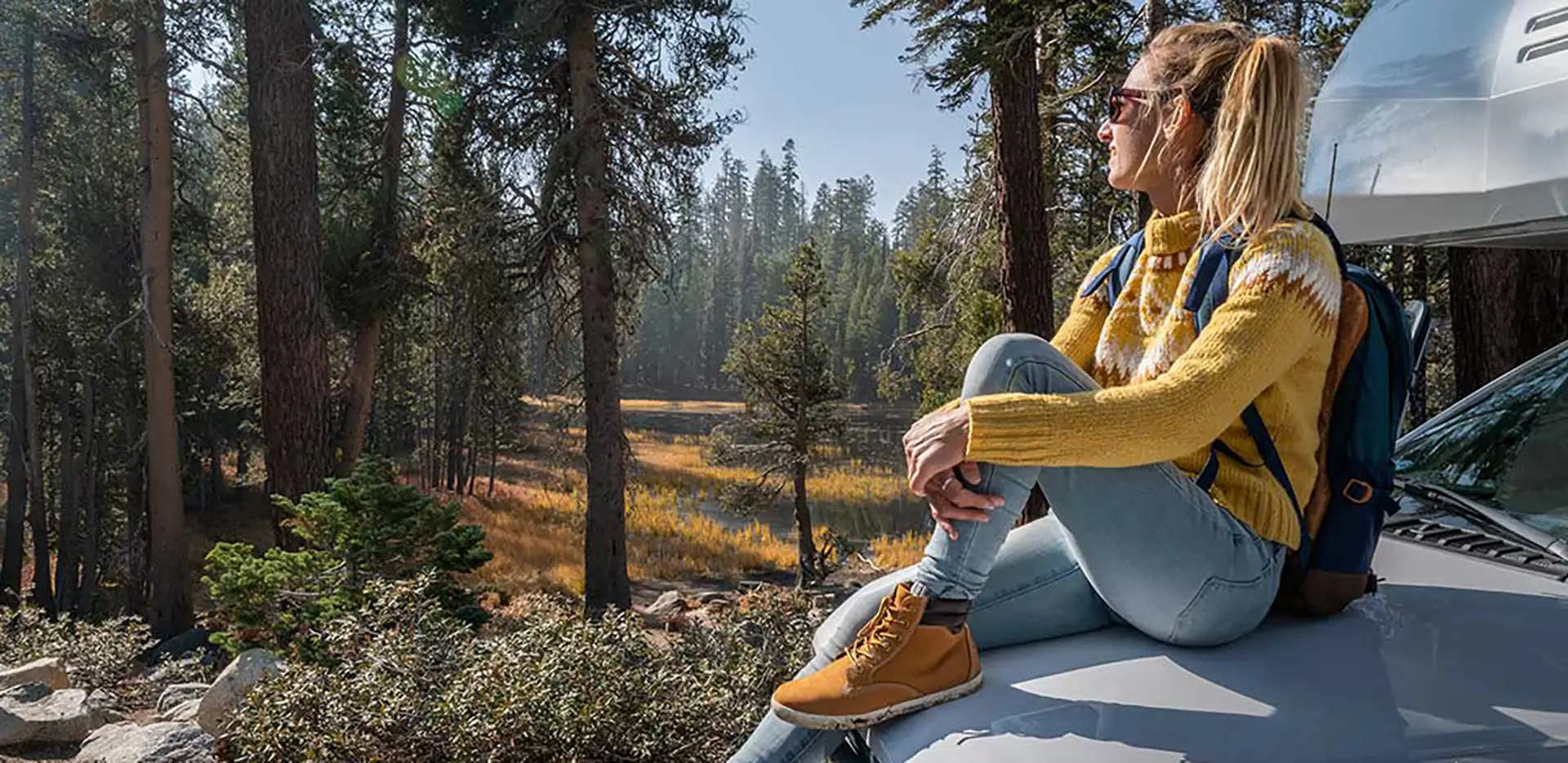 A woman sitting on the front hood of a camper van.