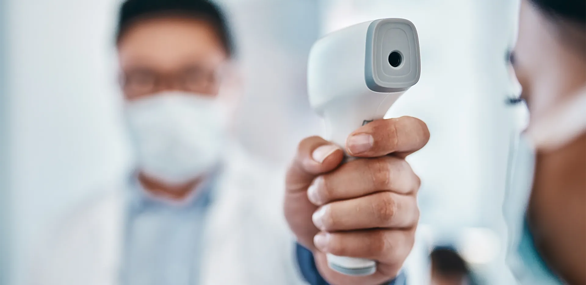 A medical professional wearing a mask takes a patient's temperature.