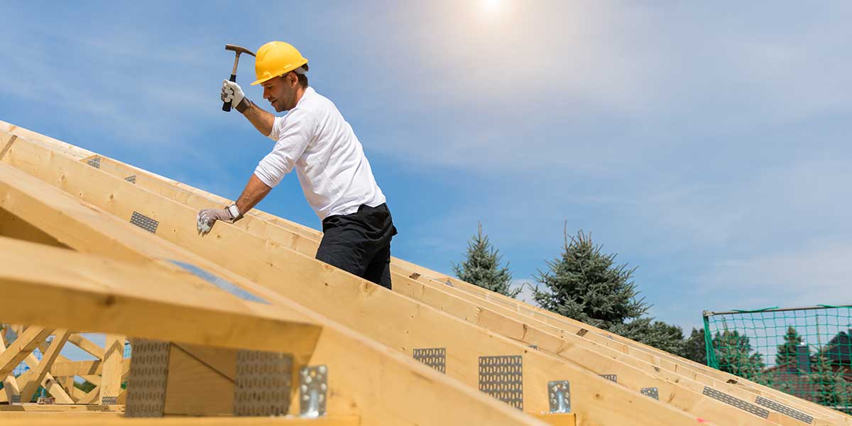 A construction worker holding a hammer up on a the framing of a house under construction.