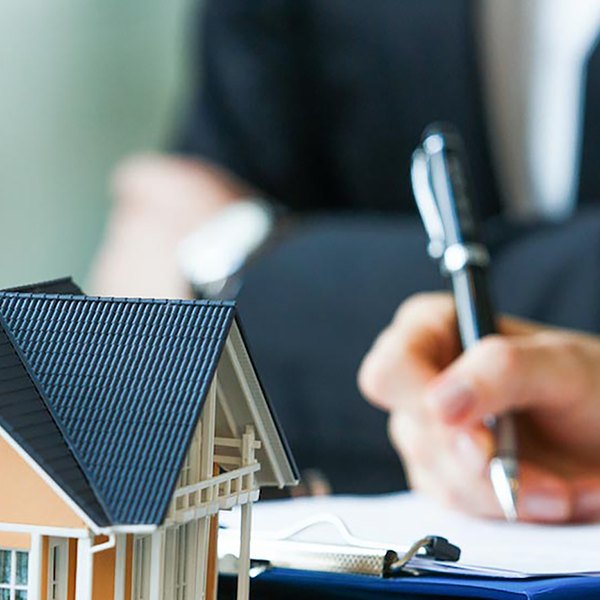 A small model of a home in front of someone signing documents on a clipboard.