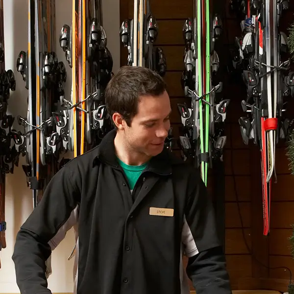 A man wearing a nametag standing in front of a wall of skis.