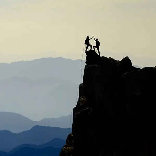 A pair of climbers in silhouette high-fiving at the top of a cliff.