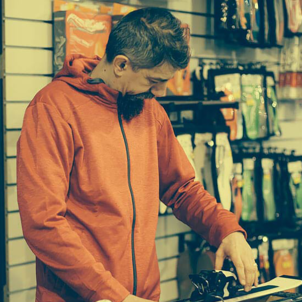 A man in an orange sweater repairing a pair of skis in a ski shop.
