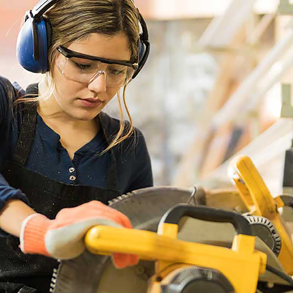 A woman wearing earmuffs operating a buzz saw.