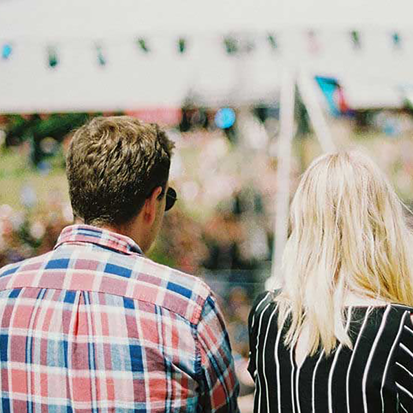 A trio of people standing in front of an out-of-focus tent and crowd.
