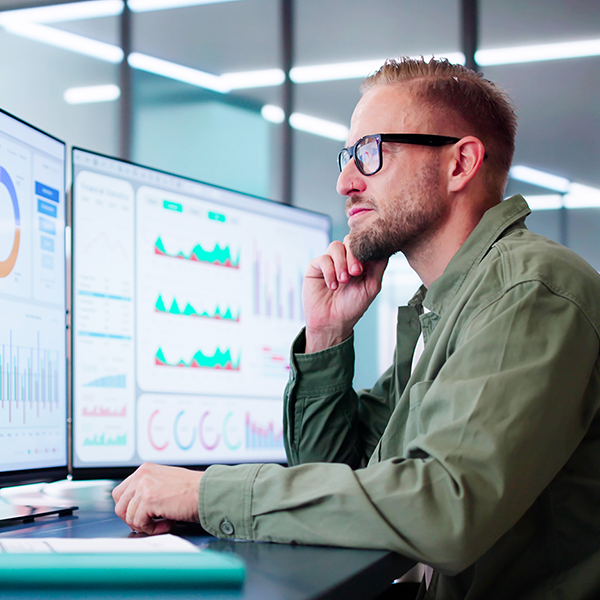 A professional sitting in front of a pair of computer monitors showing assorted graphs.