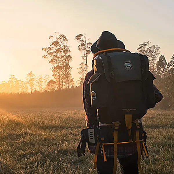 A person wearing a backpacking backpack looking at the sunset.