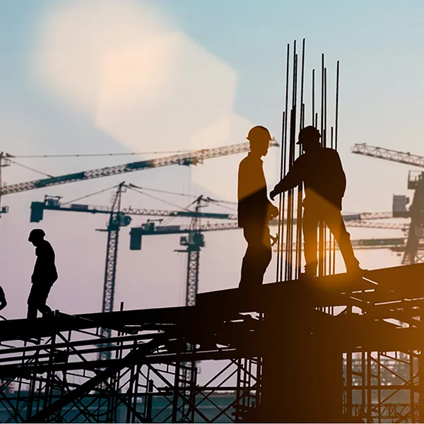 Silhouettes of a group of construction workers with cranes in the background.