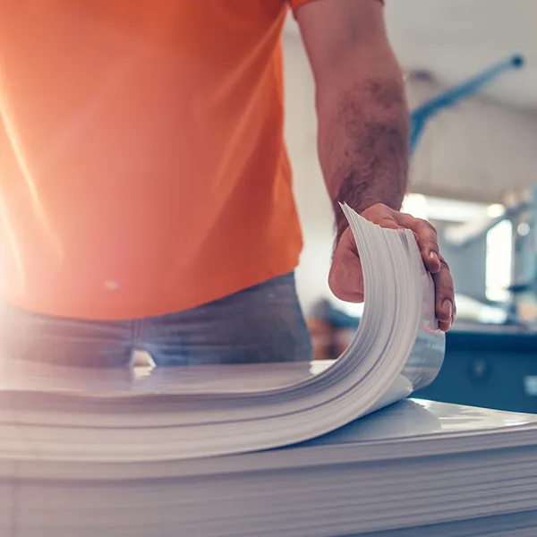 A person in an orange t-shirt flipping through a stack of paper.