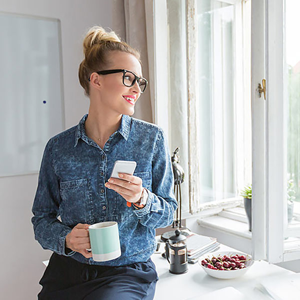 A woman holding her cell phone and looking out the window.