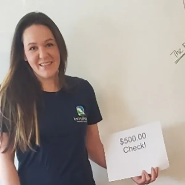 An InterWest team member handing a piece of paper reading '$500 Check' to a member of the Butte Humane Society.