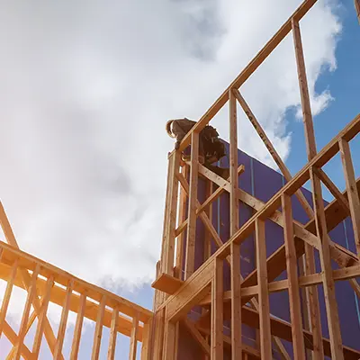 A worker climbing atop the framework of a house under construction.