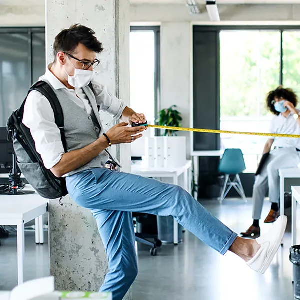 A pair of office workers wearing masks stretching a tape measure between them.