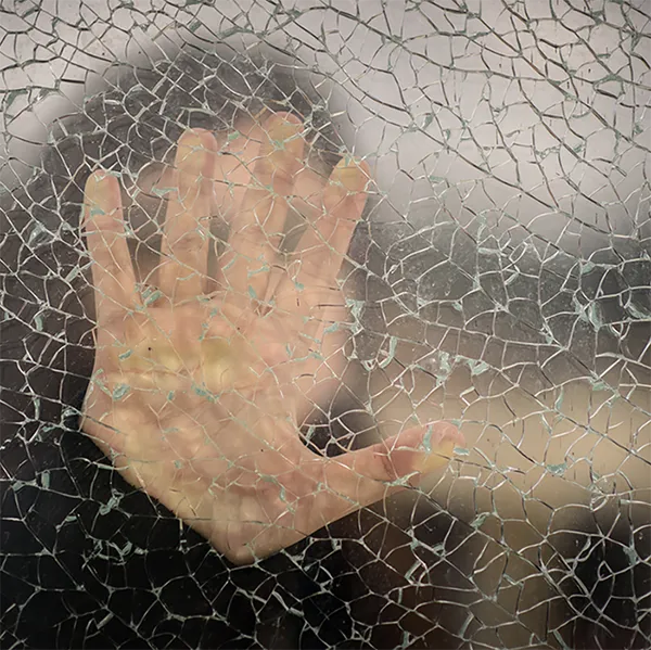 A hand against glass with cracks running through it.
