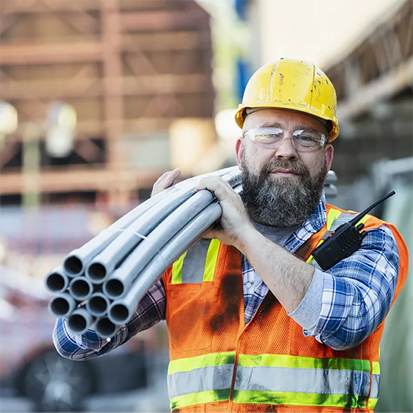A construction worker carrying a bundle of PVC pipes.