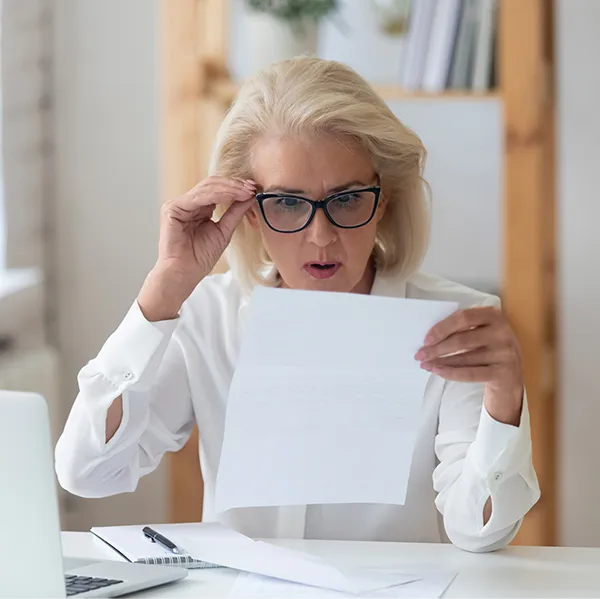 A woman looking at a piece of paper looking shocked.