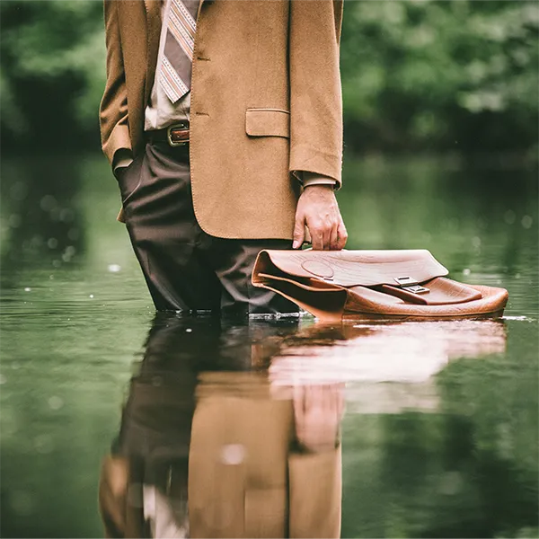 A business person standing in water up to their knees, with their briefcase by their side.