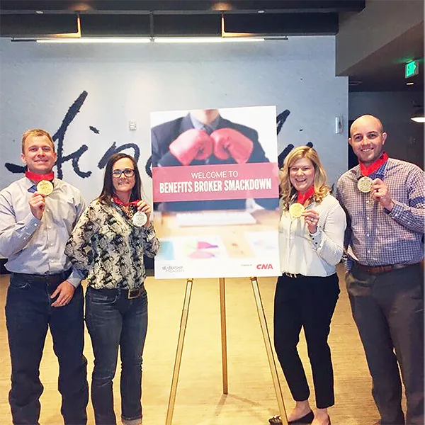 InterWest team members holding up gold medals in front of a sign reading 'Welcome to Benefits Broker Smackdown.'