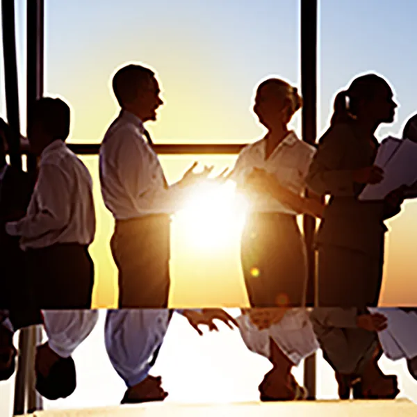 Business people talking next to a conference table in front of a large window.
