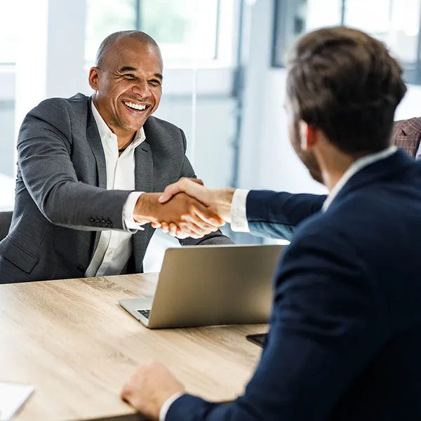 Two businessmen shaking hands while their colleagues look on.