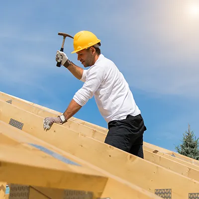 A construction worker holding a hammer up on a the framing of a house under construction.