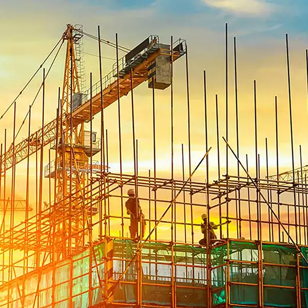 Two construction workers on scaffolding with cranes in the background.
