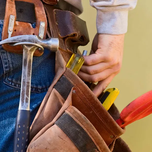 A close-up of a contractor grabbing a tool from a pouch at their hip.