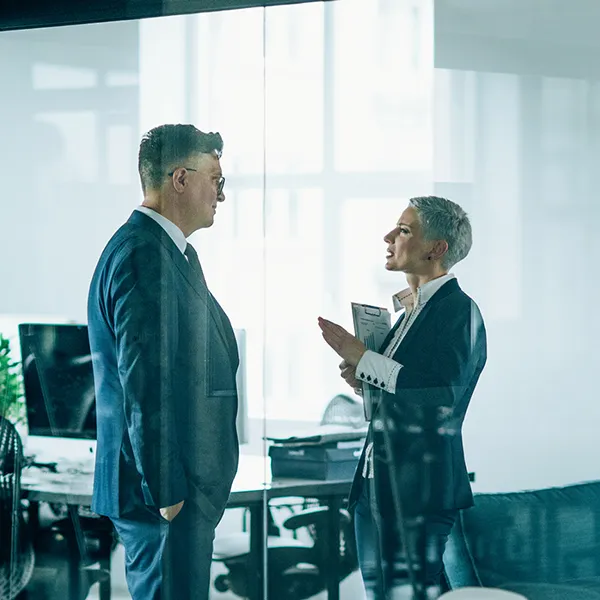Two business people wearing suits speak in an office building.