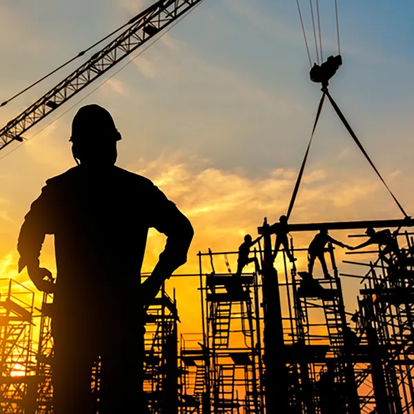 Silhouettes of construction workers on scaffolding at sunset.