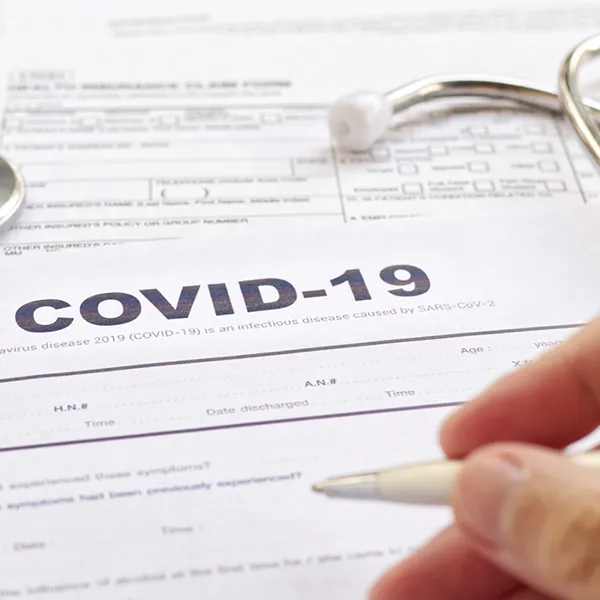 A hand signing paperwork that reads 'COVID-19' at the top.