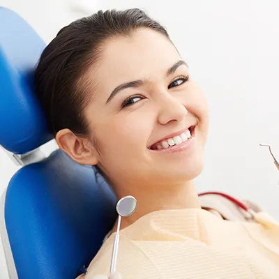 A young woman in a dentist's examination chair smiling at the camera.