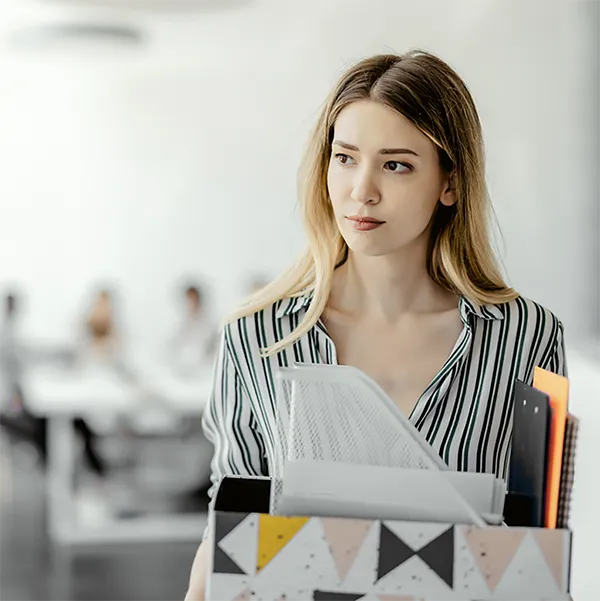 A professionally dressed woman carrying a box of supplies from her desk.