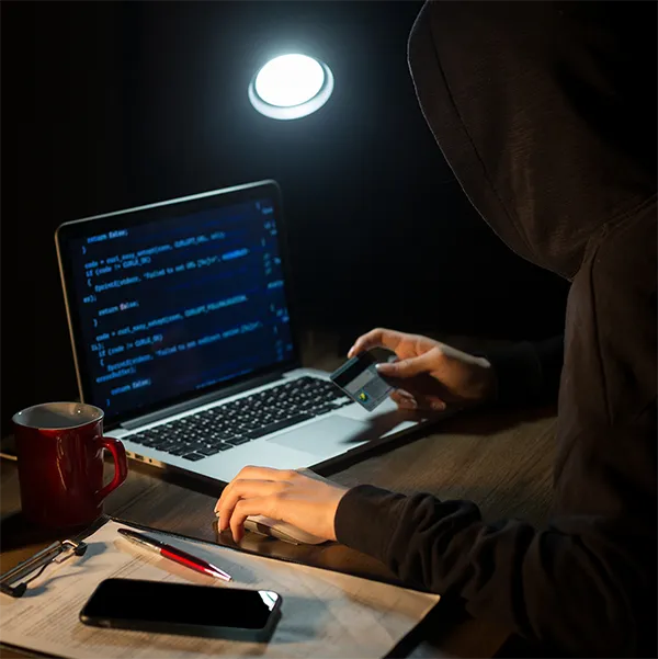 A person sitting in shadow looking at code on a laptop computer.